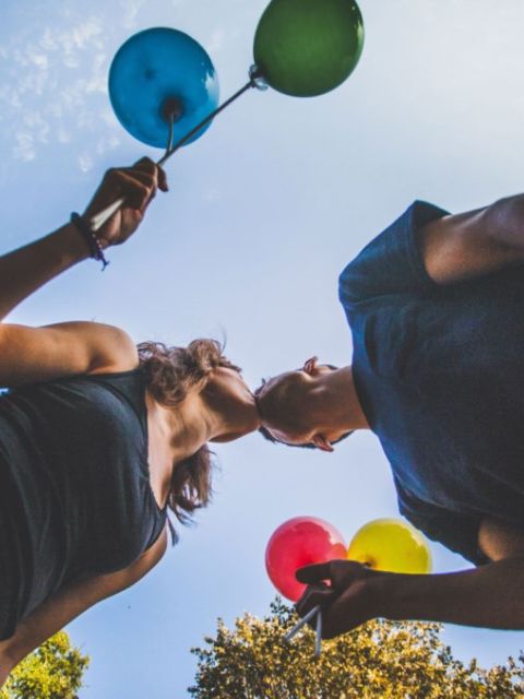 relation fluide et équilibrée couple qui s'embrasse, vu d'en bas, la fille et le garçon tiennent chacun deux ballons