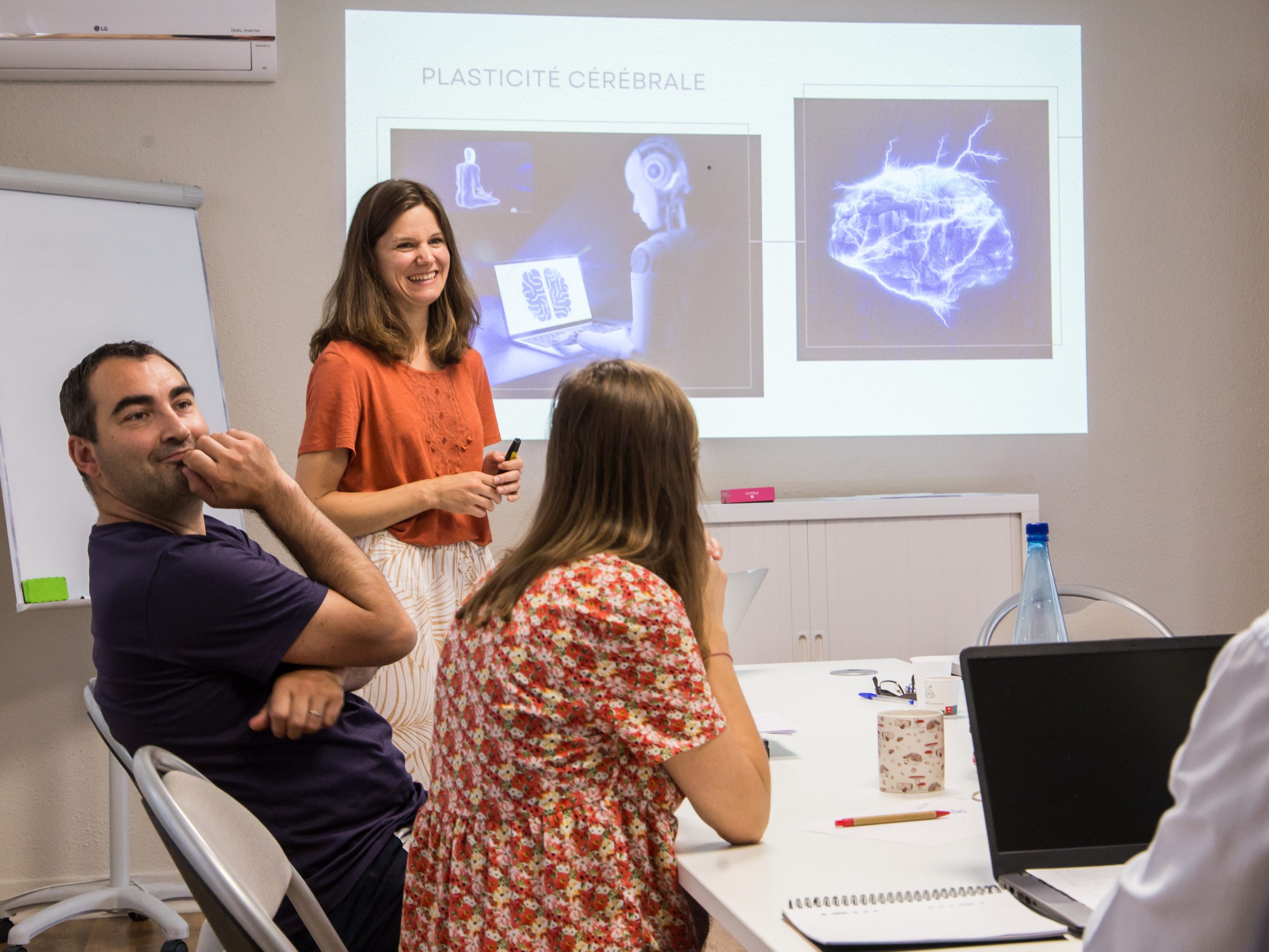 Femme devant power point et personnes autour d'une table pour regarder