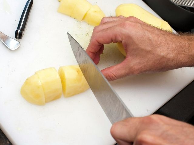 Mains qui coupent des patates sur une planche